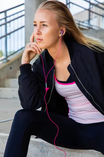 Pensativo Fit Mujer escuchando música mientras está sentado en los pasos —  Fotos de Stock