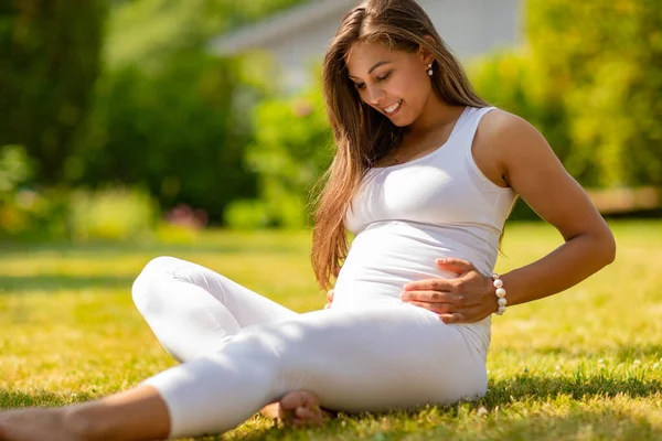 Sorridente donna incinta seduta sull'erba nel suo giardino — Foto Stock
