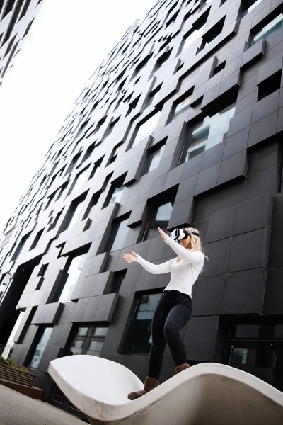 Frau mit Virtual-Reality-Brille zwischen futuristischen Stadtgebäuden — Stockfoto