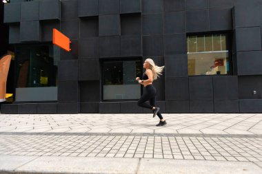 Minimalist şehir ortamında koşan sportif genç bayanın yan görünüşü