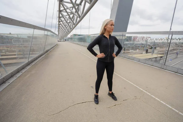 黒のワークアウトで金髪の女性の美しさは市モダンな橋に立っているを着用します。 — ストック写真