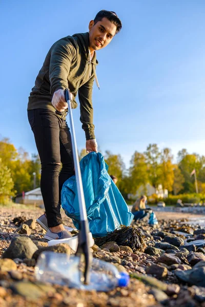Voluntario recogiendo basura con agarrador en la playa — Foto de Stock