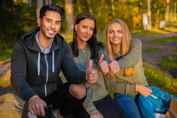 Gülümseyen genç gönüllüler parkta başparmaklarını gösteriyorlar.