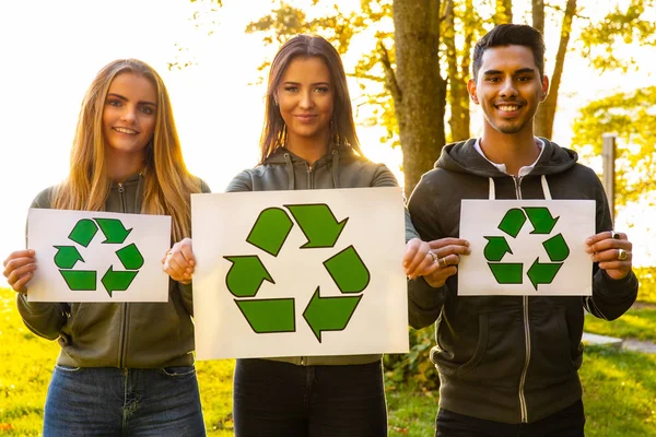 Young volunteers holding recycling symbol placard outdoor