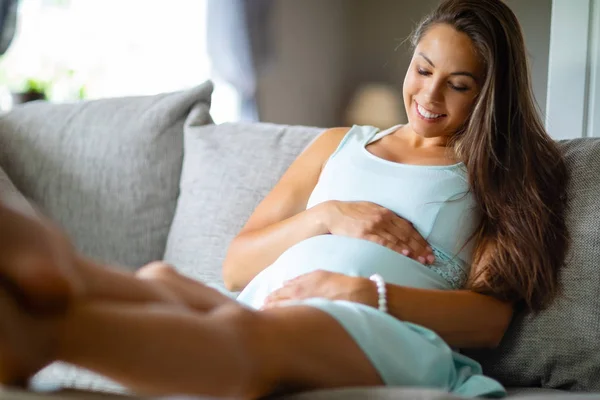 Положительная беременная женщина в платье лежит на диване дома — стоковое фото