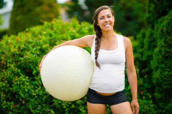 Mosolygó fiatal várandós anya gazdaság gyakorlat labda a parkban — Stock Fotó