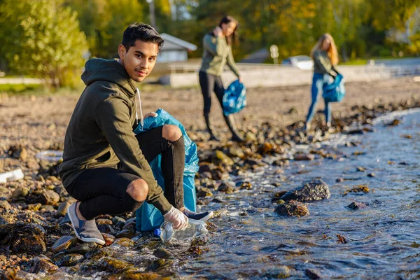 Homme accroupi tout en ramassant des ordures sur le rivage — Photo