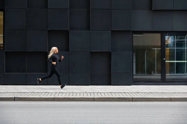 Vue latérale de la jeune coureuse sportive dans un environnement urbain minimaliste — Photo