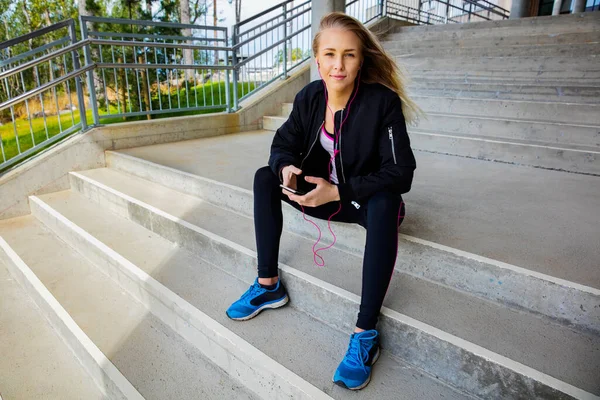 Mujer joven en ropa deportiva escuchando música en Smartphone —  Fotos de Stock