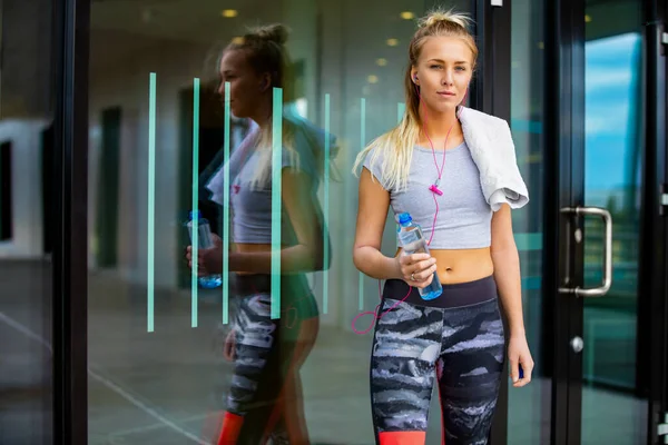 Deportiva mujer con botella de agua y servilleta de pie contra la pared — Foto de Stock