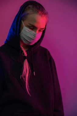Yorgun ve depresif bir kadın koruyucu yüz maskesi takmış, çok renkli ışıkları var.
