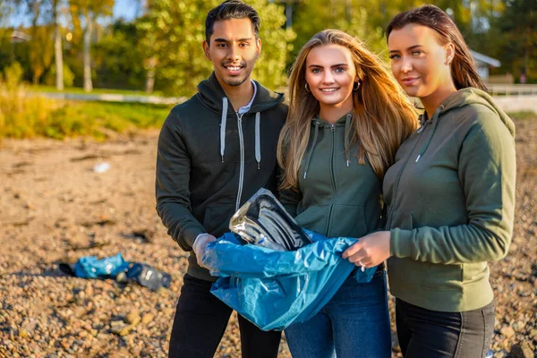 Des bénévoles souriants tenant un sac poubelle à la plage — Photo