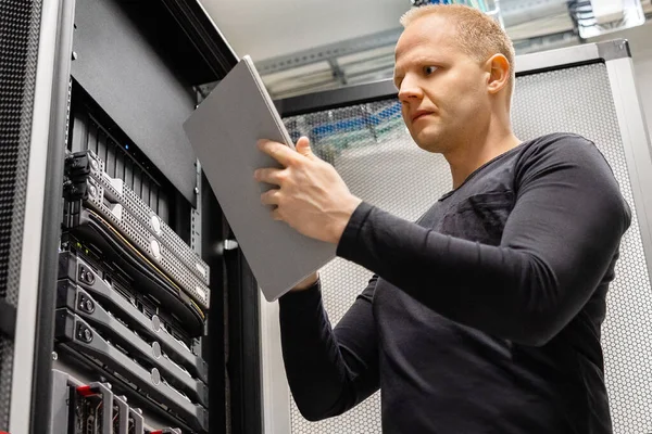 Técnico de TI masculino sosteniendo tabletas digitales analizando servidores en el centro de datos —  Fotos de Stock
