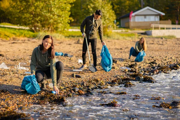 Mujer joven en un equipo recogiendo basura en una bolsa en la playa —  Fotos de Stock
