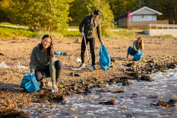 Mujer joven en un equipo recogiendo basura en una bolsa en la playa Imagen de archivo