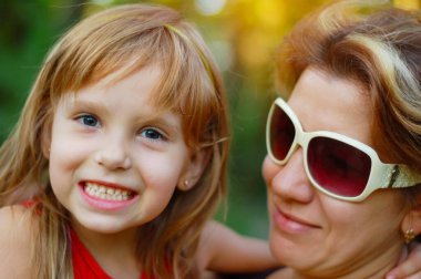 Mutlu anne parkta komik bir kızla yürüyor. Annem onu kollarında tutuyor.