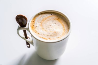 Sütlü kremalı kahve, beyaz bardakta, kaşıkla..