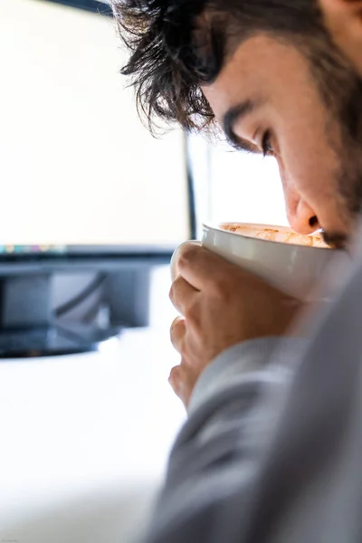 Person drinking coffee from a cup in front of the computer on a desk.