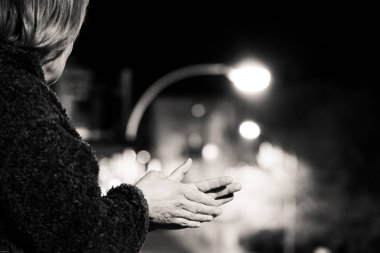 Balkonda Coronavirus 'a karşı savaşan tıbbi personeli alkışlayan siyah beyaz bir kadın resmi. Sağlık hizmetlerini ve kendilerini Coronavirus 'a feda edenleri alkışlamaya gittiler..