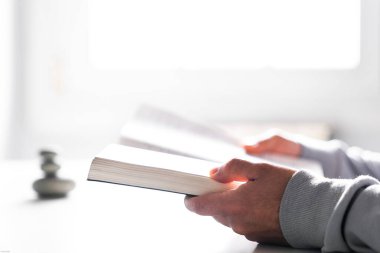 Penceresinde beyaz ışık olan bir kitap okuyorum. İki elinde de bir kitap tutuyor..