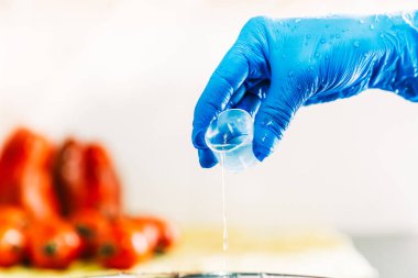 Hand with blue latex gloves pouring disinfectant liquid to decontaminate fruit and vegetables from viruses. Washing the fruit with bleach. clipart