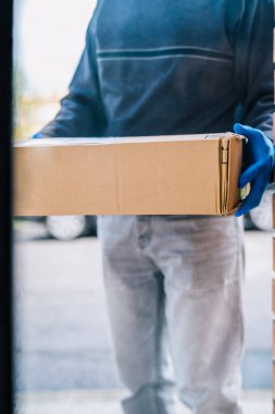 Kurtarıcı, Coronavirus 'a karşı bir önlem olarak müşterinin kapısına bir paket bırakıyor. Mavi lateks eldivenli bir eve paket teslim etmek..