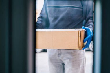 Kurtarıcı, Coronavirus 'a karşı bir önlem olarak müşterinin kapısına bir paket bırakıyor. Mavi lateks eldivenli bir eve paket teslim etmek. Teslimatçı adam camdan içeri girdi..