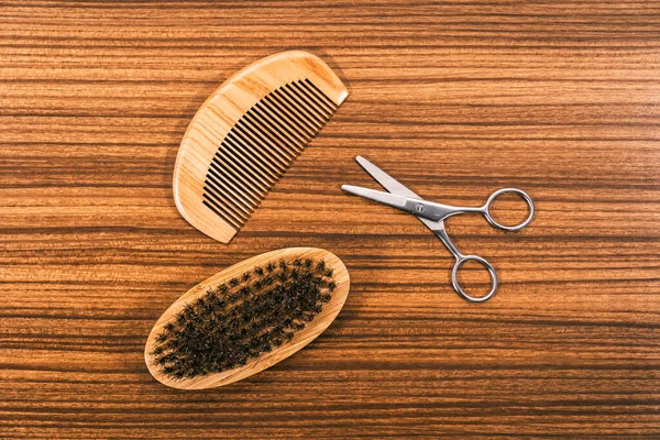 Set of tools to cut your hair and fix your beard on a vintage wooden base. Modern wooden comb, beard brush and small metal scissors.