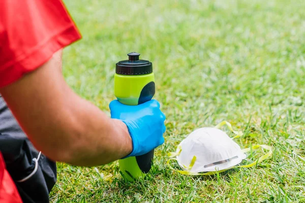 Person doing sport in the park resting while drinking water. Person doing sport with a mask to prevent the spread of the coronavirus.