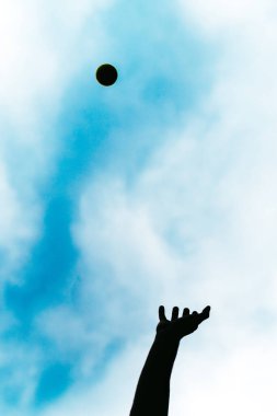 Havaya top atarak spor yapan mutlu insan. Güneşli bir yaz gününde bir tenis topuyla oynayan kaygısız bir insanın silueti..