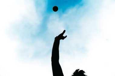 Havaya top atarak spor yapan mutlu insan. Güneşli bir yaz gününde tenis topuyla oynayan kaygısız bir çocuğun silueti..