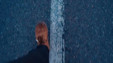 Kahverengi deri çizmeli bir insanın ayak manzarası asfalt beyaz bir çizgi üzerinde yürüyor..