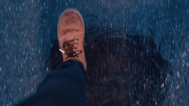 道路上のアスファルトの水たまりの上を歩く濡れた茶色の革のブーツで人の足のゼニスビュー — ストック動画