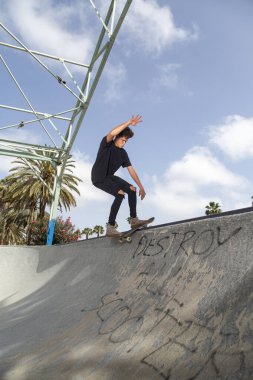 Genç kaykaycı, sokak arkaplanı ve mavi gökyüzü ile parkta numaralar yapıyor..