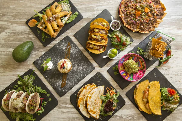 Yukarıdan görülen tipik Meksika yemekleriyle dolu bir masa. Nacho, taco, chimichanga, quesadilla, guacamole.