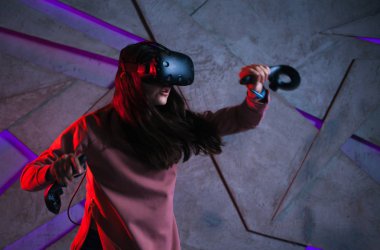 Kılıç kullan. Sanal kasklı genç bir kadın, sanal kılıçların kolları gibi her iki elinde de kontrolörler kullanır..