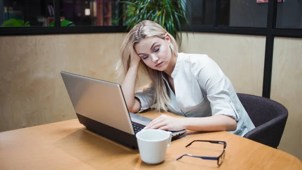 Unavená přepracovaná mladá žena v kanceláři u notebooku — Stock fotografie