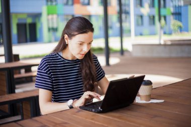 Bir esmer kız ahşap masanın arkasında oturur, bir dizüstü bilgisayar monitörü bakar, gülümsüyor, güler, online görüşmeler, içecekler kahve, çalışır.