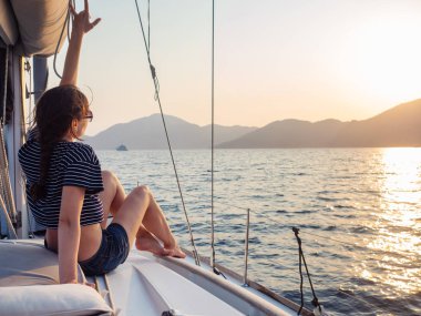 çizgili bir t-shirt çekici genç kadın bir yelkenli yat güvertesinde gün batımı sahiptir. Yelkenli yarış