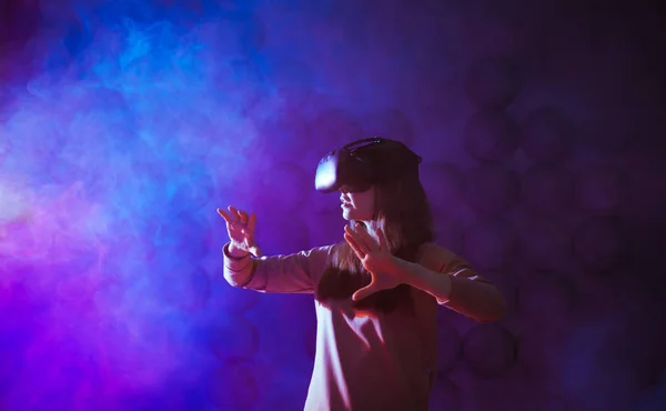 Começa a viagem. Mulher jovem surpreendente tocando ar durante a experiência VR contra neon e fumaça de fundo futurista . — Fotografia de Stock