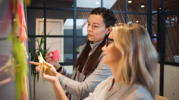 Takım çalışması, proje yönetimi, çevik yöntem. Ofiste iki genç iş kadını var.