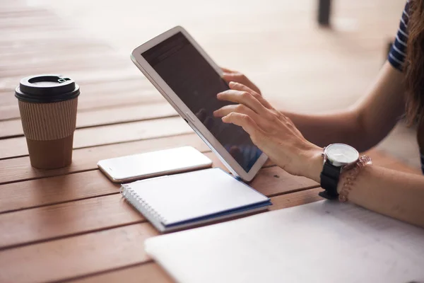 Women\'s hands with neat manicure and large wristwatch, work with gadgets, tablet, smartphone, papers on a wooden table.