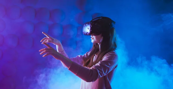 Mulher jovem surpreendente tocando o ar durante a experiência VR contra neon e fumaça de fundo futurista . — Fotografia de Stock