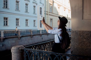 Şehirde turist Smartphone bir fotoğraf çeker. Siyah şapkalı genç bir kadın ve beyaz bir gömlek,