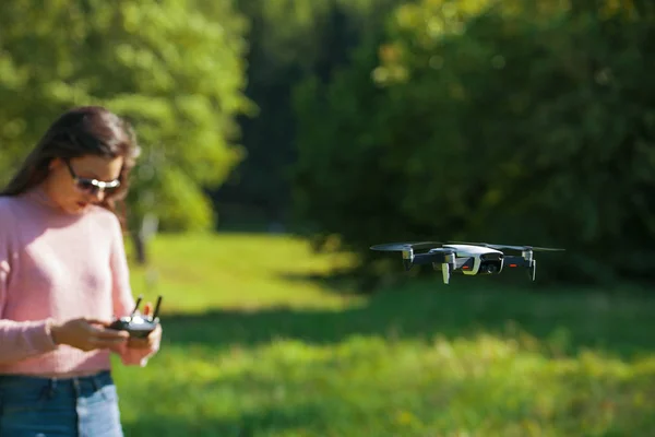 El dron de cuatro hélices flotaba en el aire a nivel de los ojos. La mujer está vigilando su vuelo con un panel de control . —  Fotos de Stock