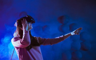 Yolculuk başlıyor. VR deneyimi sırasında neon ve duman fütüristik arka plana karşı havaya dokunan genç kadın hayret verici..