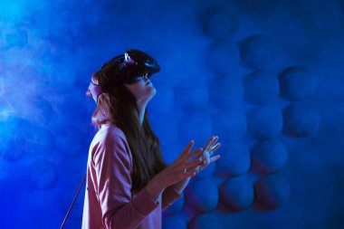 Yolculuk başlıyor. VR deneyimi sırasında neon ve duman fütüristik arka plana karşı havaya dokunan genç kadın hayret verici..