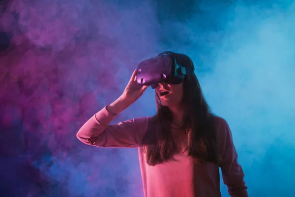 Uma jovem usa óculos, capacete de realidade virtual em um fundo de fundo escuro em fumaça. Corrige os óculos . — Fotografia de Stock