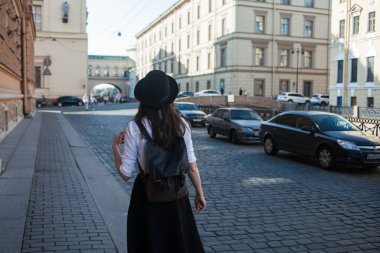 Şapkalı genç bir kadın şehrin arka manzarasında yürüyor. Kız turist yürüyüşü seviyor..