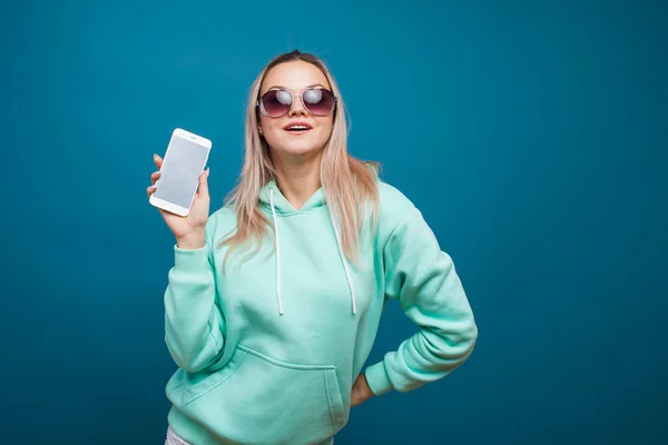 Elegante moderno hipster menina com capuz azul com o capuz usa um smartphone. — Fotografia de Stock